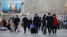 Passagiere mit Gesichtsmasken gehen mit ihrem Gepäck vor dem Pekinger Bahnhof in Peking spazieren. Foto: epa/Wu Hao