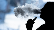 Eine junge Frau raucht mit einer E-Shisha und ist dabei als Silhouette zu sehen. Foto: Silas Stein/dpa