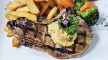 Das gegrillte Schweinskotelett wird mit hausgemachter Kräuterbutter, Pommes frites und Buttergemüse serviert. Bild: Jaybee'Swiss Restaurant