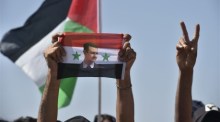 Ein Mensch hält eine syrische Flagge mit einem Foto von Präsident Bashar Assad in die Höhe, während arabische Jugendliche an einem Sommerlager teilnehmen. Archivfoto: epa/WAEL HAMZEH