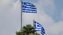 Zwei griechische Nationalflaggen wehen vor einem bewölkten Himmel im Wind. Foto: Anna Ross/dpa