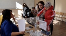 In einem Wahllokal während der Parlamentswahlen in Custendil hält eine Frau ihr Kind, um den Stimmzettel abzugeben. Foto: epa/Georgi Licovski