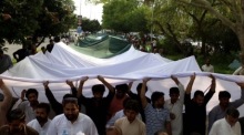 Menschen tragen eine große pakistanische Flagge, während sie vor den Feierlichkeiten zum Unabhängigkeitstag in Islamabad auf einer Straße marschieren. Foto: epa/Sohail Shahzad