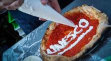Ein Pizzabäcker schreibt den Schriftzug "Unesco" auf eine Pizza. Italiens Regierung rührt die Werbetrommel für die «cucina italiana». Foto: picture alliance/Cesare Abbate/ansa/ap/dpa