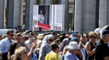Gläubige stehen in der Nähe eines großen Bildschirms, auf dem zu sehen ist, wie Papst Franziskus das sonntägliche Angelusgebet auf dem Petersplatz spricht. Foto: epa/Riccardo Antimiani