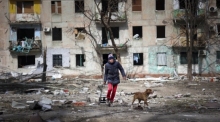 Ein Mann geht mit seinem Hund in der Nähe eines Wohnhauses entlang, das durch den Beschuss von Kämpfen am Stadtrand von Mariupol in der Ukraine beschädigt wurde. Foto: Alexei Alexandrov/Ap/dpa