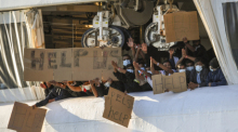 Migranten halten Transparente mit der Bitte um Hilfe an Deck des unter norwegischer Flagge fahrenden Schiffes «Geo Barents», das von «Ärzte ohne Grenzen» betrieben wird, im Hafen von Catania. Foto: Salvatore Cavalli/Ap/dpa