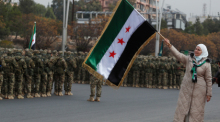 Bei Feiern in Damaskus schwenkt eine Frau die syrische Flagge, während Soldaten der neuen Armee ein Jahr nach Assads Sturz Aufstellung nehmen. Foto: dpa/Omar Sanadiki