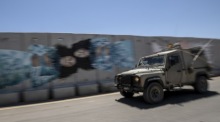 Ein israelisches Militärfahrzeug fährt an einem Graffiti an der Sicherheitsmauer vorbei, die in der Nähe des israelischen Moshavs Shtula an der israelisch-libanesischen Grenze errichtet wurde. Foto: epa/Atef Safadi