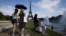 Frauen suchen unter einem Sonnenschirm am Trocadéro-Brunnen am Eiffelturm in Paris Schutz vor der Hitze. Foto: epa/Yoan Valat