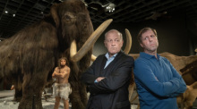 Privatdetektiv Wilsberg (Leonard Lansink) steht Rücken an Rücken mit Ekki (Oliver Korittke) in einem Raum eines Naturkundemuseums, im Hintergrund steht ein großes ausgestopftes Mammut. Foto: Thomas Kost/Zdf/dpa