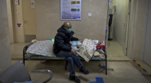 Ein Mann mit Mund-Nasen-Schutz kümmert sich um seinen älteren Verwandten, der in einem Korridor der Notaufnahme eines Krankenhauses intravenöse Infusionen erhält. Foto: Andy Wong/Ap/dpa