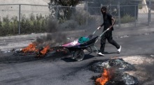 Ein Mann schiebt einen Wagen an Reifen vorbei, die von Demonstranten während einer Demonstration in Port-au-Prince in Brand gesetzt wurden. Foto: epa/Johnson Sabin