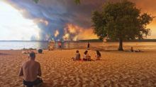 Strandbesucher sitzen am Strand von Moutchic in Lacanau im Südwesten Frankreichs, während Rauchwolken von einem Waldbrand in den Himmel aufsteigen. Foto: Maximilien Lamy/Afp/dpa