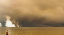 Ein Strandbesucher spaziert am Strand von Moutchic in Lacanau, während Rauchwolken eines Waldbrands aufsteigen. Foto: dpa/Maximilien Lamy