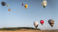 Heißluftballons fliegen während der 1. Fahrt der Deutschen Meisterschaft über einem Feld und werfen über einem Zielkreuz farbige Marker ab. Foto: Daniel Vogl/dpa