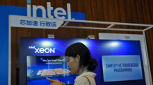 Eine Frau schaut auf ihr Smartphone in der Nähe eines Intel-Standes, der für Xeon-Chips wirbt. Foto: Andy Wong/Ap/dpa