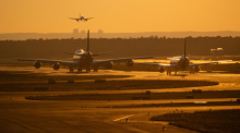 Flugzeuge rollen im Licht der untergehenden Sonne zu ihrer Parkposition auf dem Flughafen Frankfurt, während eine weitere Maschine zur Landung ansetzt. Foto: Boris Roessler/dpa