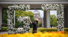 Ein Gärnter arbeitet im Hiroshima Peace Memorial Park an einem G7 Logo aus Blumen mit dem Genbaku Dome im Hintergrund. Foto: Michael Kappeler/dpa
