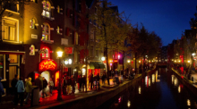 Menschen schlendern am Abend an einer Gracht entlang durch den Rotlichtbezirk De Wallen. Foto: Koen Van Weel/epa/dpa