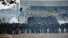 Anhänger des ehemaligen brasilianischen Präsidenten Bolsonaro (hinten) geraten in der Hauptstadt mit Ordnungskräften aneinander, die hinter Absperrungen eine Kette bilden und Tränengasgranaten auf die Demonstranten ab... Foto: Matheus Alves./dpa