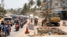 Eine Baustelle an einer belebten Ringstraße auf Koh Samui mit Staub, Baggern und wartenden Motorrollern im Gegenlicht. Foto: Der Farang (ai)