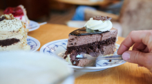 Eine Frau sticht mit der Kuchengabel in ein Stück Torte, während eine weitere Stückchen Torte auf dem Tisch in einem Café stehen. Foto: Annette Riedl/dpa