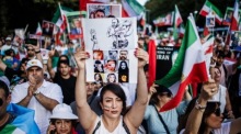 Eine Demonstrantin hält ein Blatt mit Fotos von Opfern, darunter Jina Mahsa Amini. Foto: epa/Clemens Bilan