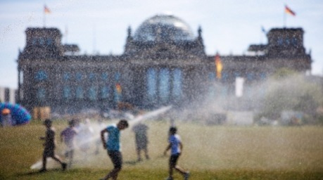 Menschen kühlen sich an Wassersprinklern vor dem Reichstagsgebäude in Berlin während der Hitzewelle ab. Foto: EPA/Clemens Bilan