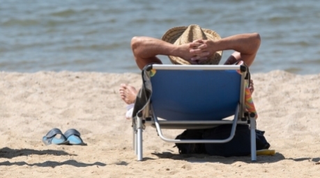 Ein Mann liegt mit einem Sonnenhut auf einer Sonnenliege am Ufer des Bärwalder See am Strand. Foto: Sebastian Kahnert/dpa-zentralbild/dpa