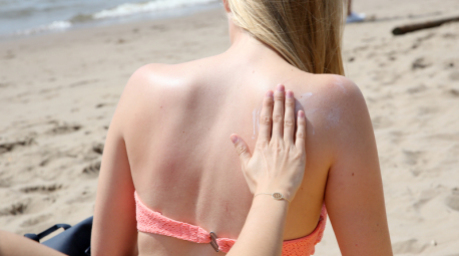 Eine junge Frau wird bei hochsommerlichen Temperaturen von ihrer Freundin mit Sonnencreme eingerieben. Foto: Bodo Marks/dpa