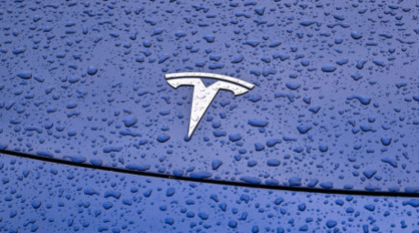 Regentropfen sind auf einem Pkw mit dem Tesla-Symbol vor dem Werk der Tesla-Autofabrik zu sehen. Foto: Patrick Pleul/dpa