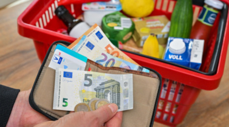 Eine Frau hält auf ihrer Hand Geld vor einem vollen Einkaufskorb mit Lebensmitteln. Foto: Patrick Pleul/dpa