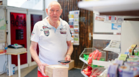 Der 83-jährige Christian Lange hält in seiner Paketannahmestelle ein Paket in den Händen. Foto: Uwe Anspach/dpa
