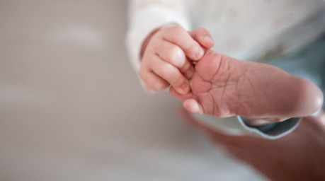 Ein Baby greift mit den Fingern nach seinem Fuß. Foto: Fabian Strauch/dpa