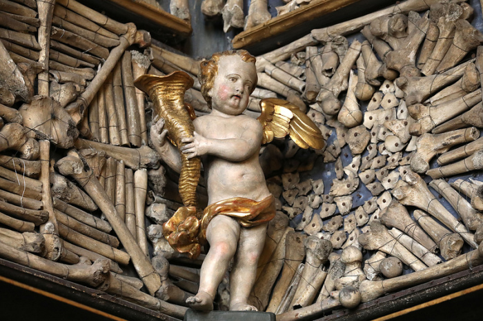 Eine Engelsfigur steht in der Knochenkammer der Kirche St. Ursula vor Gebeinen, die an der Wand befestigt sind. Foto: Oliver Berg/Dpa