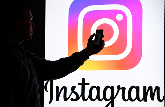 Ein Mann hält ein Smartphone vor einem Monitor mit dem Logo von Instagram. Foto: Carsten Rehder/Dpa