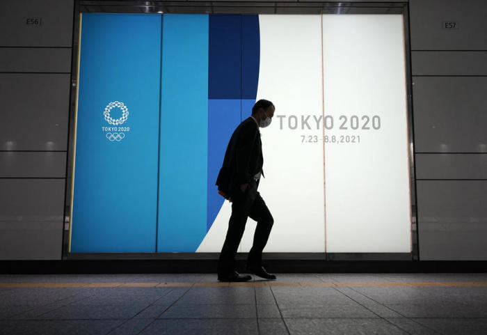 Ein mit einer Schutzmaske bekleideter Passant geht in Tokio an einer Werbetafel für die verschobenen Olympischen Spiele vorbei. Foto: epa/Franck Robichon