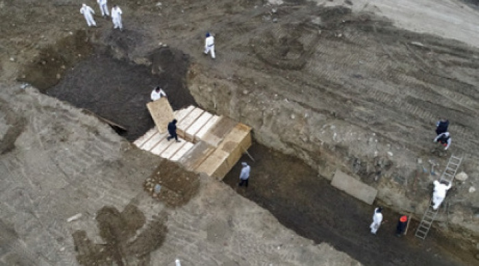Arbeiter in Schutzanzügen vergraben einfache Holzsärge in einem Graben auf Hart Island in der Bronx. Der Landstreifen auf der kleinen Insel soll als Lösung für vorübergehende Begräbnisse für Corona-Tote dienen. Die ... Foto: John Minchillo/Ap/dpa