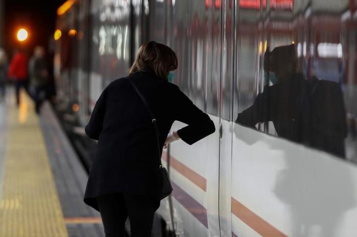 Eine vermummte Pendlerin öffnet die Türen des Zuges mit dem Ellbogen an einem Bahnsteig des S-Bahnhofs Nuevos Ministerios in Madrid. Foto: epa/Mariscal