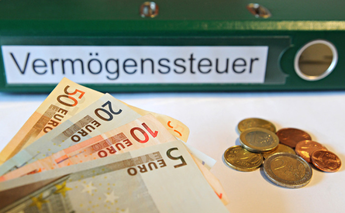 Ein Ordner mit der Aufschrift «Vermögenssteuer» liegt hinter Geldmünzen und Geldscheinen. Foto: Daniel Bockwoldt/Dpa
