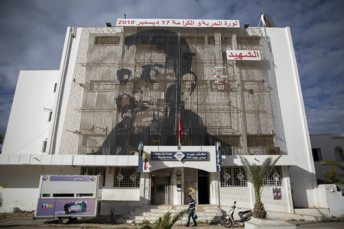 Auf der Fassade eines Postamtes in der tunesischen Kleinstadt Sidi Bouzid ist das Gesicht des tunesischen Gemüsehändlers Mohammed Bouazizi abgebildet, der sich am 17. Dezember 2010 selbst anzündete. Foto: Riadh Dridi/Ap/dpa