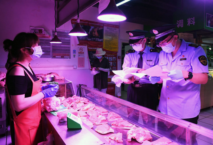 Mitarbeiter der Marktregulierungsverwaltung überprüfen an einem Marktstand im Stadtteil Haidan die Lieferkette für Fleisch und die Einhaltung von Desinfektions-Maßnahmen, die aufgrund der Corona-Pandemie getroffen wer... Foto: Ren Chao/Xinhua/dpa