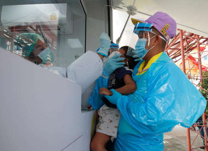 Ein Mitarbeiter eines Gesundheitsdienstes hält ein kleines Mädchen in seinem Arm, das auf Covid-19 gestetet wird. Foto: epa/Rungroj Yongrit