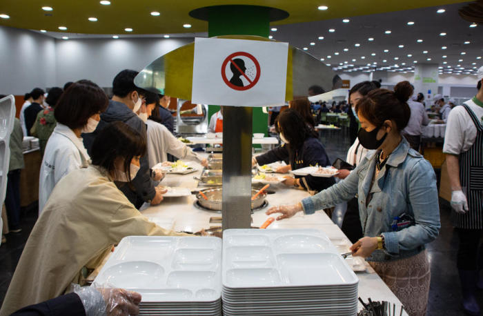 Menschen mit Masken und Handschuhen stehen in der Cafeteria des Rathauses von Seoul in Seoul Schlange, um Essen zu bekommen.