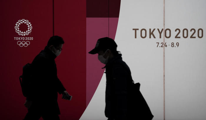 Fussgänger, die Schutzmasken tragen, gehen in Tokio am Emblem der Olympischen Spiele Tokio 2020 vorbei. Foto: epa/Kimimasa Mayama