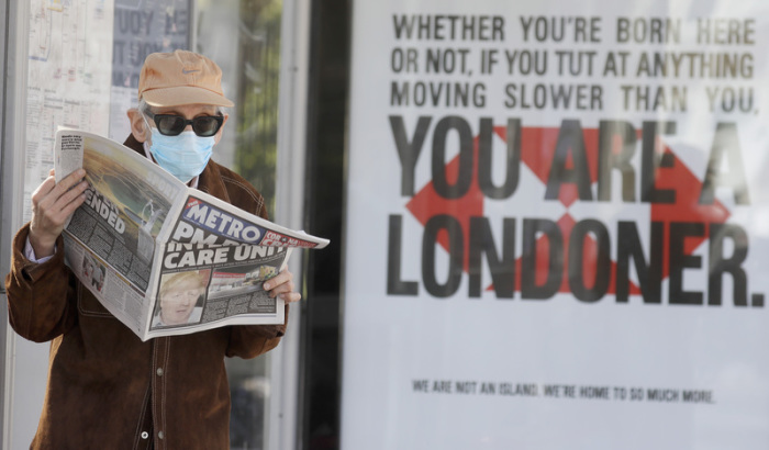 Ein Mann mit Mundschutz liest eine Zeitung mit der Schlagzeile «PM in intensive care». Der britische Premierminister Johnson ist wegen seiner Covid-19-Erkrankung auf die Intensivstation verlegt worden. Foto: Kirsty Wigglesworth/AP/dpa