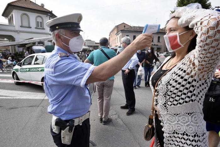 Ein Stadtpolizist, der eine Gesichtsmaske trägt und ein Gerät benutzt, überprüft die Körpertemperatur einer Frau auf dem Markt von Treviglio in der Nähe von Bergamo. Foto: epa/Yonhap