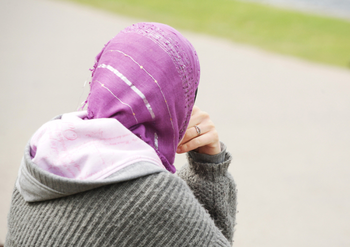 Eine junge Frau mit Kopftuch sitzt an einem Weg. Foto: Wolfram Steinberg/dpa