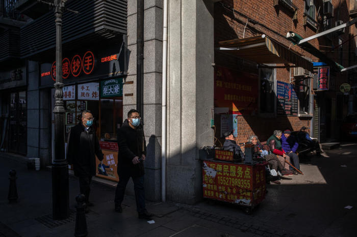 Menschen mit Gesichtsschutzmasken gehen an älteren Menschen vorbei, die sich auf einer Bank in Wuhan ausruhen. Foto: epa/Roman Pilipey